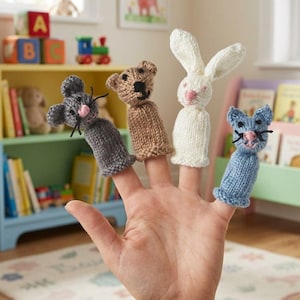 Könnte beinhalten: Eine Hand zeigt vier gestrickte Fingerpuppen: eine graue Maus, ein brauner Bär, ein weißes Kaninchen und eine blaue Katze. Jede Puppe hat gestickte Gesichtsmerkmale. Die Puppen sind für Kinderspiele und zum Geschichtenerzählen konzipiert.