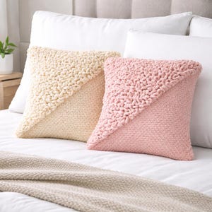 Könnte beinhalten: Zwei quadratische Zierkissen auf einem Bett. Ein Kissen ist cremefarben mit einem diagonalen strukturierten Design, das andere ist hellrosa mit einem ähnlichen Design. Eine beige Decke liegt am Fußende des Bettes.