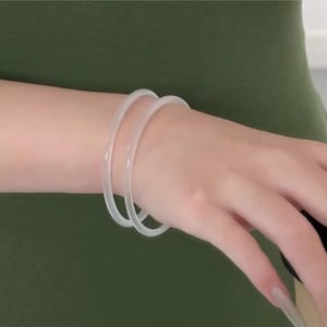 Puede incluir: Dos pulseras translúcidas y claras se llevan en la muñeca. Las pulseras son simples, redondas y parecen estar hechas de un material flexible. El fondo es de color verde oliva liso.