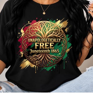Può includere: Una t-shirt nera con una grafica circolare dorata di un albero con radici. Il testo recita UNAPOLOGETICALLY FREE Juneteenth 1865. Il design è accentuato da schizzi di vernice rossa, verde e dorata dietro l'emblema centrale dell'albero.