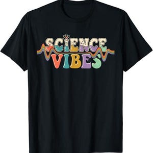 Pode incluir: Uma t-shirt preta de manga curta com o texto SCIENCE VIBES numa fonte arredondada multicolorida. O design inclui um pequeno ícone de átomo acima da palavra SCIENCE e uma linha ondulada multicolorida que separa as duas palavras.