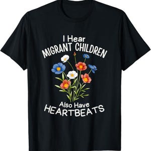 Könnte beinhalten: Ein schwarzes Kurzarm-T-Shirt mit einer bunten Blumenstrauß-Grafik in der Mitte. Der Text "I Hear MIGRANT CHILDREN Also Have HEARTBEATS" ist in weißen Großbuchstaben über und unter den Blumen aufgedruckt.