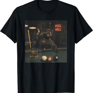 May include: A black t-shirt featuring a graphic print of a French bulldog wearing sunglasses at a pool table. The dog is positioned next to a glass of amber liquid and a pool cue. Three billiard balls are on the table, and a neon sign reads POOL HALL.
