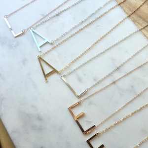 May include: A set of gold necklaces with different letter pendants. The necklaces are layered and feature a variety of chain styles.