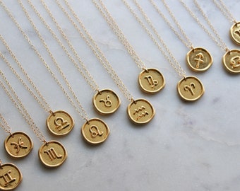 May include: Gold-colored necklaces with zodiac sign pendants. Each pendant features a different astrological symbol, such as Gemini, Libra, and Sagittarius. The necklaces are displayed on a marble surface.