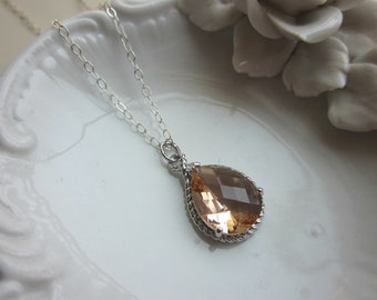 May include: A silver chain necklace with a teardrop-shaped pendant featuring a large, clear peach-colored gemstone.