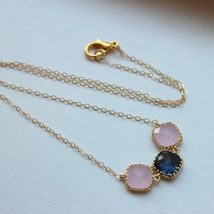 May include: A gold chain necklace with three square-shaped gemstones. The gemstones are pink and blue.