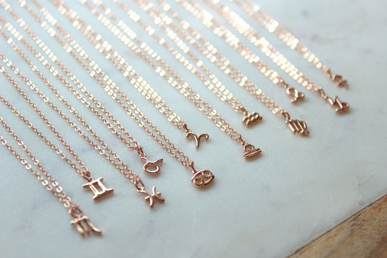 May include: A set of 12 gold-toned necklaces with zodiac signs as pendants. The signs are: Pisces, Gemini, Cancer, Leo, Virgo, Libra, Scorpio, Sagittarius, Capricorn, Aquarius, Aries, and Taurus.