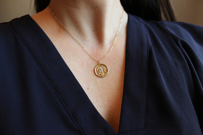 Pu&ograve; includere: Una collana con catena dorata con un ciondolo rotondo che presenta un design di scorpione dettagliato.