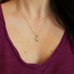 Puede incluir: Un collar de cadena dorada con un peque&ntilde;o colgante redondo que presenta un s&iacute;mbolo del zod&iacute;aco. El colgante est&aacute; detallado con un borde texturizado y un dise&ntilde;o delicado.