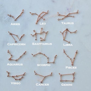 May include: Twelve gold zodiac constellation necklaces with small clear crystals. The constellations are Aries, Taurus, Gemini, Cancer, Leo, Virgo, Libra, Scorpio, Sagittarius, Capricorn, Aquarius, and Pisces.