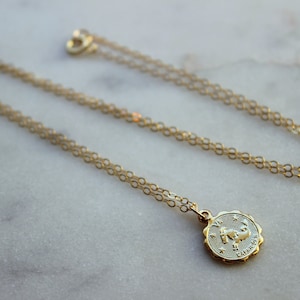 May include: A gold chain necklace with a gold pendant featuring the zodiac symbol for Cancer. The pendant is round and has a detailed design of a crab.