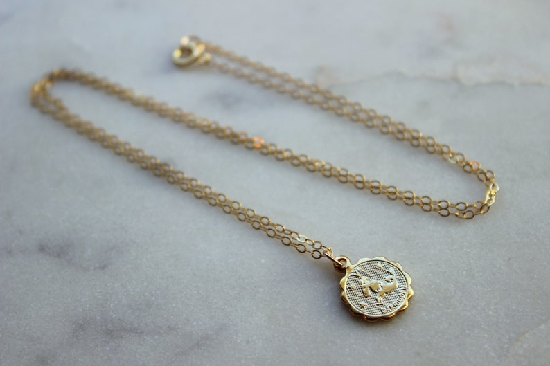 May include: A gold chain necklace with a gold pendant featuring the zodiac symbol for Cancer. The pendant is round and has a detailed design of a crab.