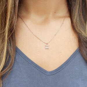 May include: A delicate rose gold necklace with a small Gemini zodiac symbol pendant.