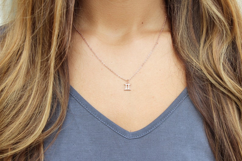May include: A delicate rose gold necklace with a small Gemini zodiac symbol pendant.