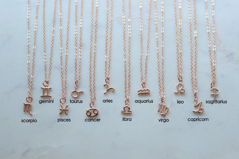 May include: Twelve gold necklaces with zodiac signs as pendants. The signs are: Scorpio, Gemini, Pisces, Taurus, Aries, Aquarius, Virgo, Leo, Capricorn, Sagittarius, Libra, and Cancer.