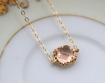 May include: A delicate gold chain necklace with a large, light pink, faceted gemstone pendant. The pendant is set in a gold crown-like setting.