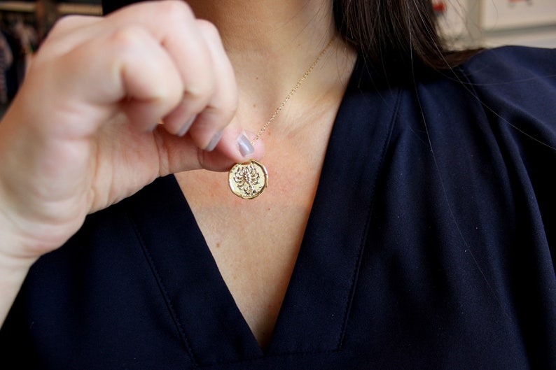 Pu&ograve; includere: Una collana d'oro con un ciondolo rotondo che presenta un design di scorpione dettagliato.
