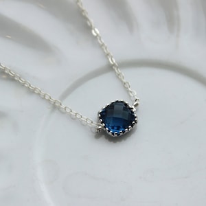 May include: A silver chain necklace with a dark blue gemstone pendant. The pendant has a scalloped edge.