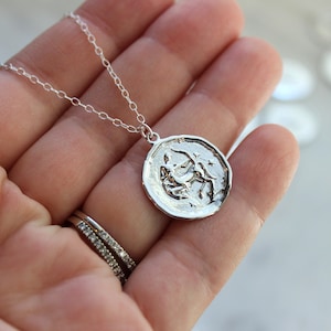 May include: A silver necklace with a round pendant featuring a detailed depiction of the Sagittarius zodiac sign.