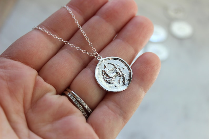 May include: A silver necklace with a round pendant featuring a detailed depiction of the Sagittarius zodiac sign.
