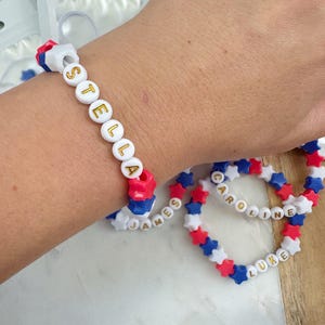 May include: Three colorful beaded bracelets with the names "Stella", "James", and "Caroline" and "Luke" spelled out in gold letters.