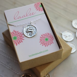 May include: A silver Sagittarius zodiac necklace in a brown gift box with a pink and green floral design. The box has the text "laalee" and "laaleejewelry.com" printed on it.