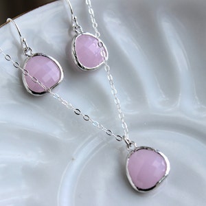 Op de afbeelding: Een zilveren ketting en oorbellen set met roze edelsteen hangers. De ketting heeft een delicate ketting en de oorbellen zijn van het druppeltype.