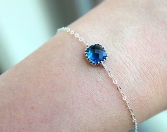 Peut inclure: Un bracelet délicat en chaîne argent avec une seule pierre précieuse ronde bleu foncé sertie dans une bélière argent.