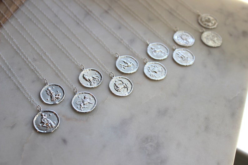 May include: A set of silver necklaces with zodiac signs pendants. Each pendant features a different zodiac symbol, including Aries, Taurus, Gemini, Cancer, Leo, Virgo, Libra, Scorpio, Sagittarius, Capricorn, Aquarius, and Pisces.
