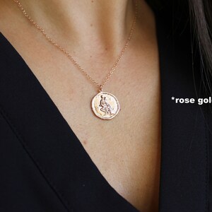 May include: A rose gold necklace with a round pendant featuring a detailed design of a woman sitting. The pendant is on a delicate chain.