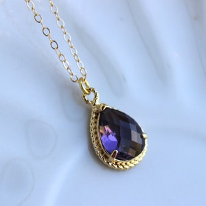 Puede incluir: Un collar de cadena dorada con un colgante en forma de lágrima que presenta una gran piedra preciosa púrpura facetada.