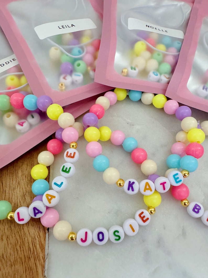 May include: Three colorful beaded bracelets with the names "Laalee", "Josie", and "Kate" spelled out in colorful letters. The bracelets are made with pastel-colored beads and gold spacers.