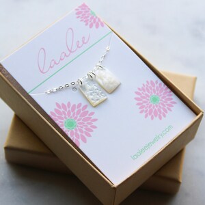 May include: A white and silver necklace with two rectangular pendants in a brown gift box. The box has a white card with the text "laalee" and "laaleejewelry.com".