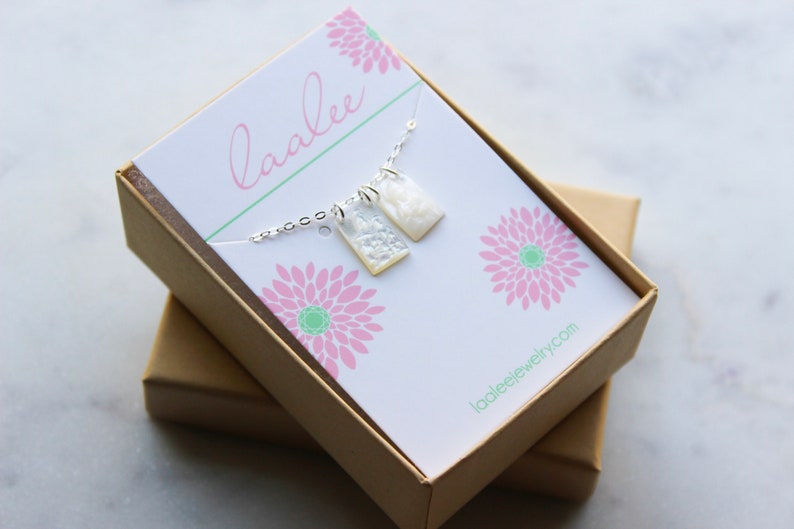 May include: A white and silver necklace with two rectangular pendants in a brown gift box. The box has a white card with the text "laalee" and "laaleejewelry.com".