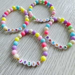 May include: Four colorful beaded bracelets with the names "KATE", "LAALE", "JOSIE", and "BRENNA" spelled out in white letters with rainbow colored outlines.