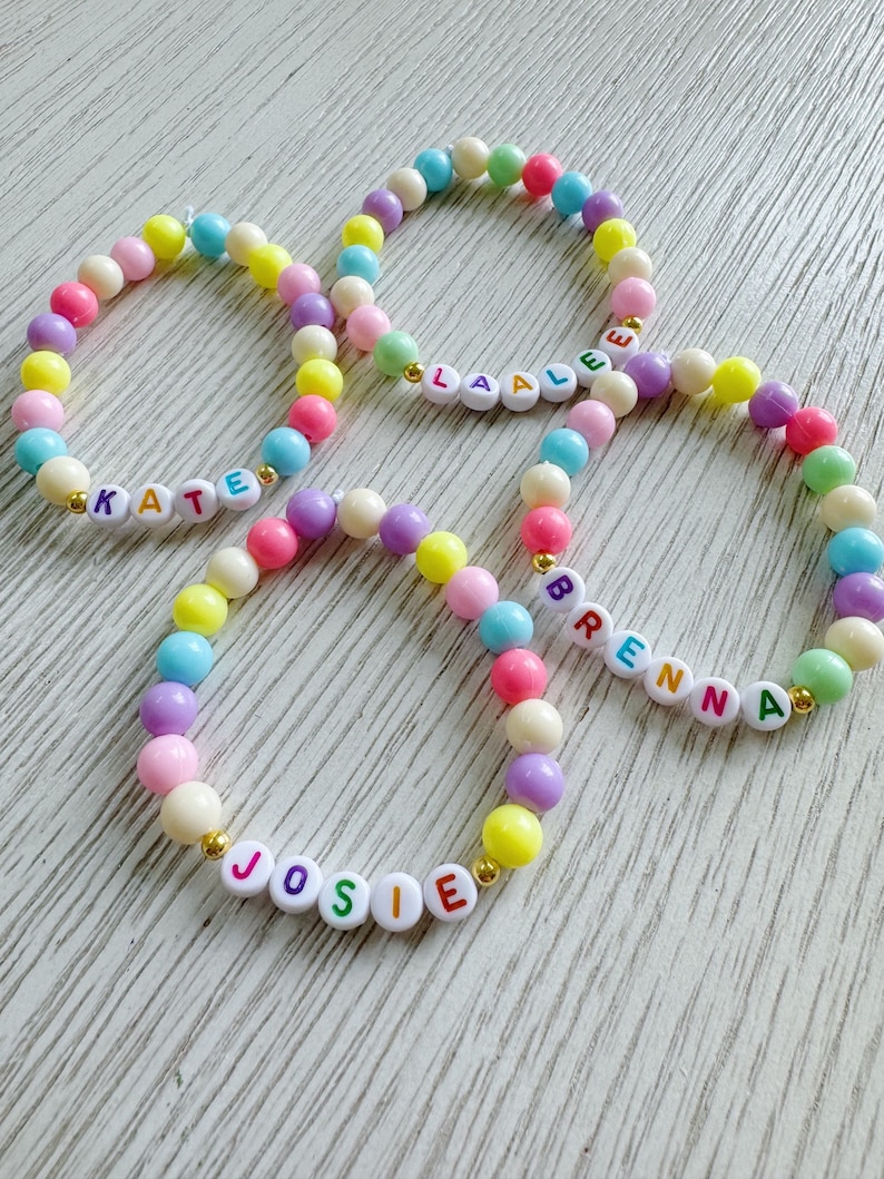 May include: Four colorful beaded bracelets with the names "KATE", "LAALE", "JOSIE", and "BRENNA" spelled out in white letters with rainbow colored outlines.