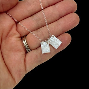 May include: A silver chain necklace with two white rectangular pendants. The pendants have a textured surface and appear to be made of mother of pearl.