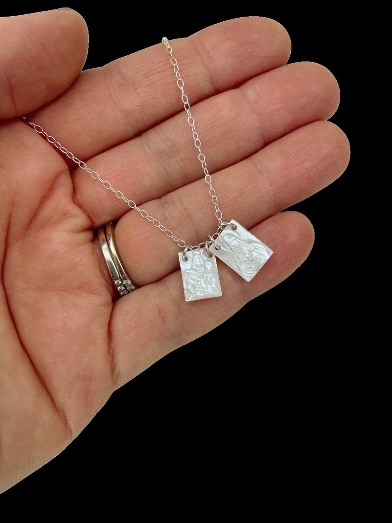 May include: A silver chain necklace with two white rectangular pendants. The pendants have a textured surface and appear to be made of mother of pearl.