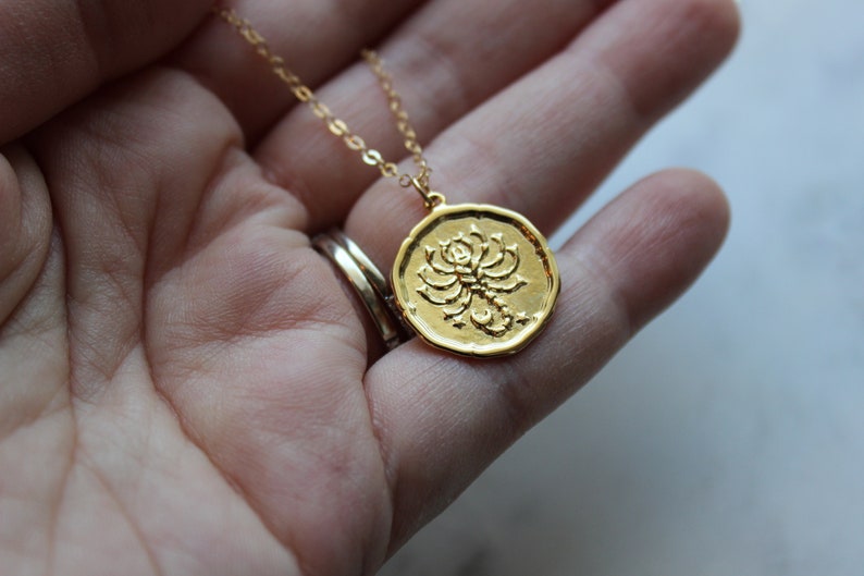 Pu&ograve; includere: Collana d'oro con un ciondolo rotondo che presenta un designo di scorpione dettagliato. Il ciondolo &egrave; testurizzato e ha un design in rilievo.