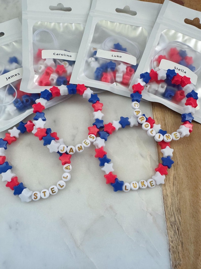 May include: Four red, white, and blue star-shaped bead bracelets with gold lettering spelling out the names "James", "Stella", "Caroline", and "Luke".