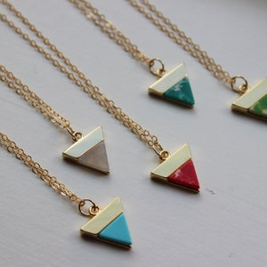 May include: Five gold necklaces with triangle pendants. Each pendant is a different colour: white, turquoise, green, red, and white. The necklaces are on a white surface.