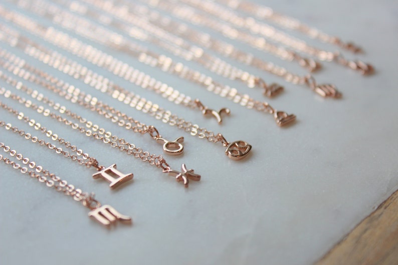 May include: A set of 12 gold-toned zodiac necklaces with delicate chains. Each necklace features a different zodiac symbol, including Gemini, Virgo, Pisces, Taurus, and Libra.