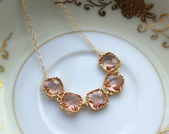 May include: A gold chain necklace with five pink faceted square-shaped stones. The necklace is on a white background.