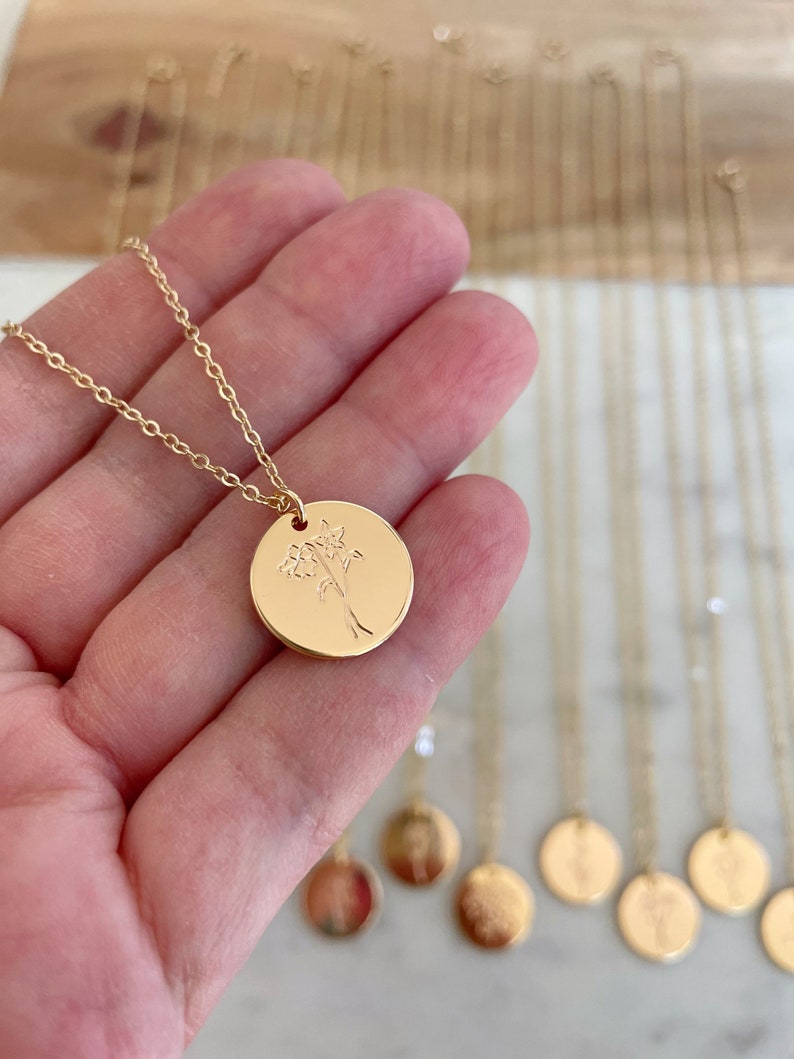 Peut inclure: Collier dor&eacute; avec un pendentif rond grav&eacute; d'un motif floral. Le pendentif est suspendu &agrave; une fine cha&icirc;ne. Plusieurs autres colliers similaires sont visibles, sugg&eacute;rant une collection de bijoux ou une pr&eacute;sentation.