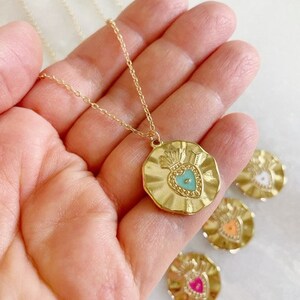 K&ouml;nnte beinhalten: Goldkette mit einem goldenen Anh&auml;nger in Form eines Herzens mit einem t&uuml;rkisfarbenen Zentrum. Der Anh&auml;nger ist von einem strukturierten, gewellten Rand umgeben. Die Kette wird auf einer Hand pr&auml;sentiert.