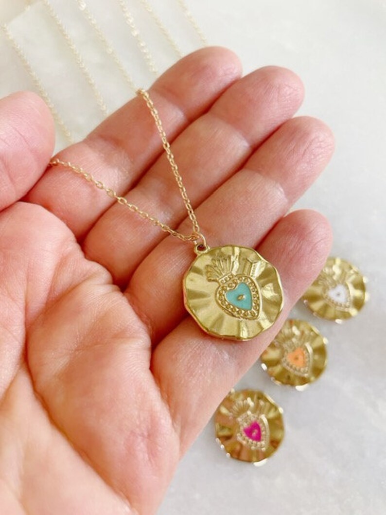 K&ouml;nnte beinhalten: Goldkette mit einem goldenen Anh&auml;nger in Form eines Herzens mit einem t&uuml;rkisfarbenen Zentrum. Der Anh&auml;nger ist von einem strukturierten, gewellten Rand umgeben. Die Kette wird auf einer Hand pr&auml;sentiert.