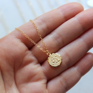 May include: Gold chain necklace with a small, round pendant featuring the zodiac symbol for Libra.