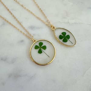 May include: Two gold necklaces with four-leaf clover charms encased in clear resin. One charm is round and the other is oval.