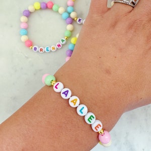 May include: Two colorful beaded bracelets with the names "Brenna" and "Laalee" spelled out in colorful letters. The bracelets are made with white beads and colorful letters.